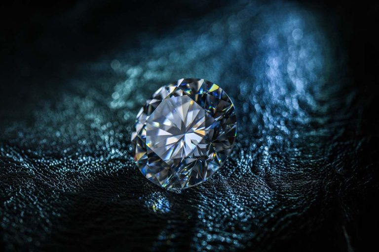 Close-up of a brilliant-cut, sparkling clear diamond resting on a textured dark surface